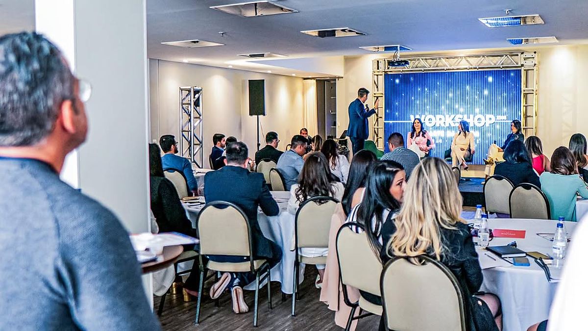Plateia sentada nas mesas acompanhando o painel do workshop